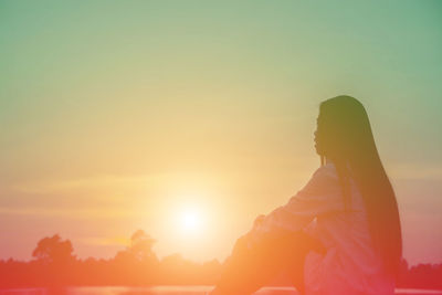 Silhouette woman standing against orange sky