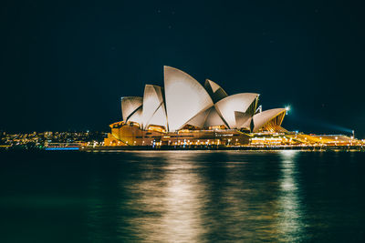 Illuminated city by sea against sky at night