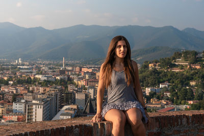 Portrait of beautiful young woman in city against mountains