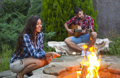 Young couple sitting on bonfire against trees