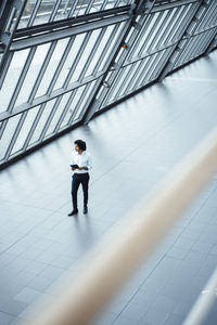 Young businessman with digital tablet walking by roof in office corridor