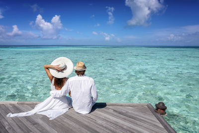 Rear view of couple sitting on pier looking at sea