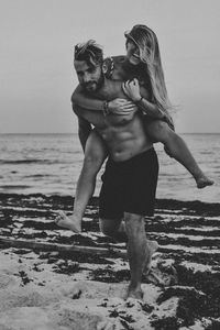 Full length of man carrying girlfriend on back at beach