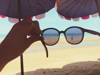 Cropped image of hand holding sunglasses on beach