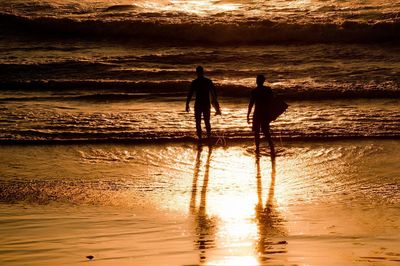 Silhouette men standing on beach during sunset