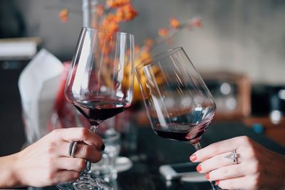 Cropped hands of women toasting red wine at restaurant