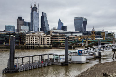 Bridge over river by buildings against sky in city