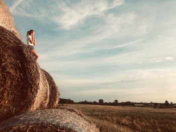 Girl standing on hay bales against sky