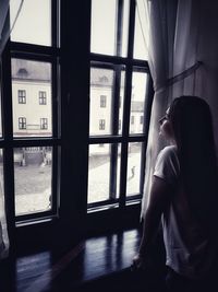 Rear view of woman looking through window at home
