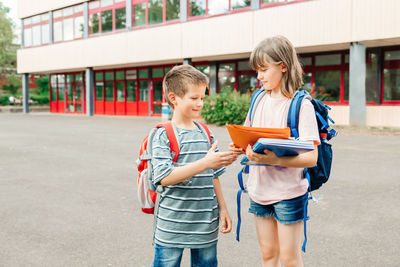 To school. brother and sister with school bags in the school yard. girl explaining homework 