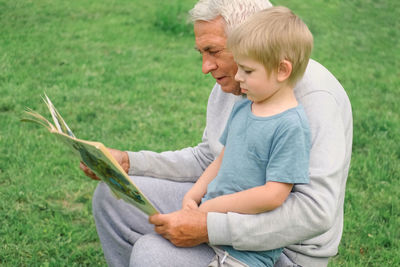 Side view of boy using mobile phone while sitting on field