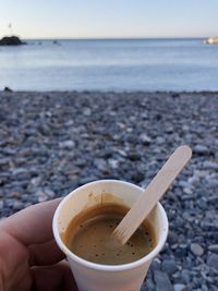 Close-up of hand holding coffee cup at beach