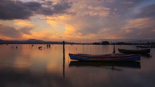 Boats moored in pond against sky during sunset