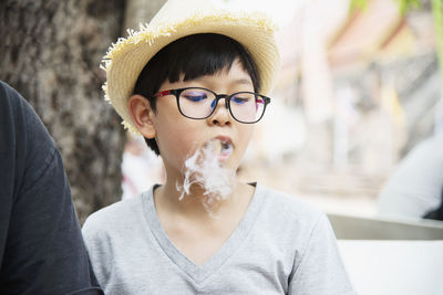 Close-up of boy emitting smoke by friend