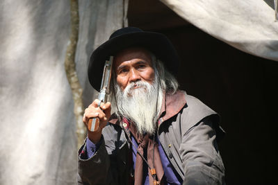 Portrait of senior man with hat holding handgun outdoors