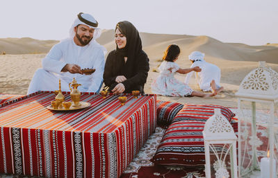 Happy family having tea on carpet at desert