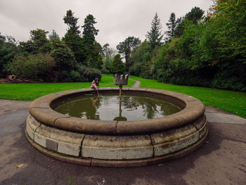 Fountain in park by lake against sky
