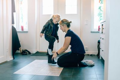 Mother helping daughter with shoes near door at home