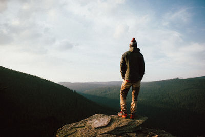 Rear view of man standing on mountain against sky