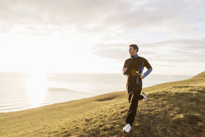 Full length of man jogging on hill by sea during sunny day