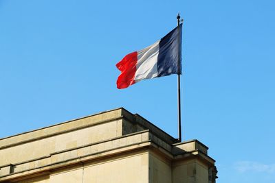 Low angle view of flag against building against clear blue sky