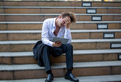 Full length of young man using mobile phone while sitting on staircase