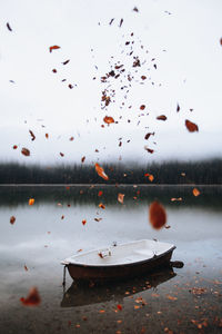 Leaves in mid-air against moored boat in lake