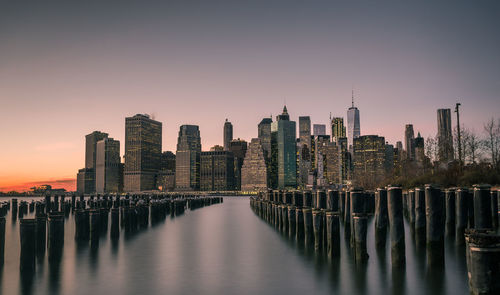 Sea by illuminated city against sky during sunset