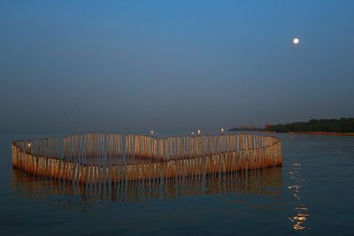 Wooden posts in sea against clear sky at night