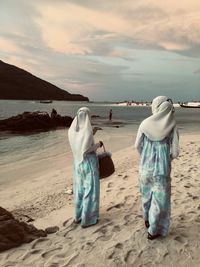 Rear view of woman standing at beach against sky during sunset