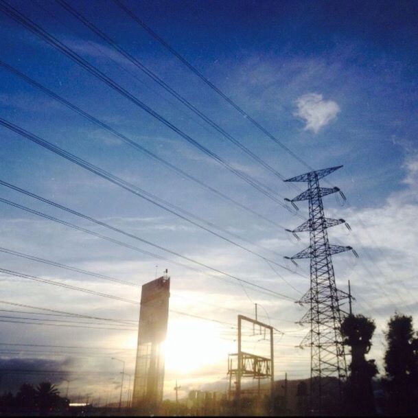 power line, electricity pylon, power supply, electricity, low angle view, fuel and power generation, sky, silhouette, connection, cable, sun, sunset, technology, sunlight, power cable, built structure, cloud - sky, sunbeam, building exterior, architecture