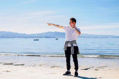 Young man on the beach using mobile phone and pointing a direction