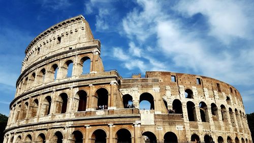 Low angle view of coliseum against cloudy sky