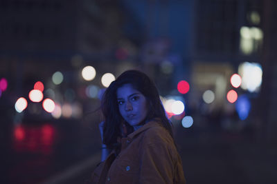 Portrait of woman standing on illuminated street at night