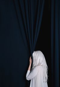 Rear view of woman hiding by curtain