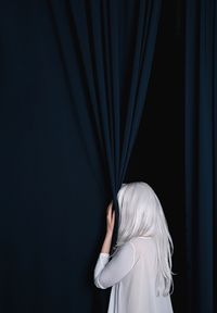 Rear view of woman hiding by curtain