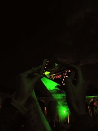 Close-up of hand holding illuminated lighting equipment against sky at night