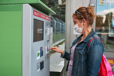 Woman buying bus ticket in ticket machine wearing face mask to cover mouth and nose