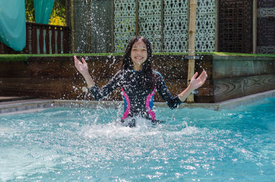 Portrait of happy girl splashing water in swimming pool