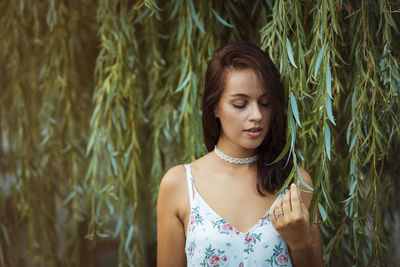 Young woman looking down while touching leaf 