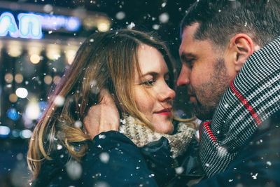 Couple romancing while standing against sky at night during snowing