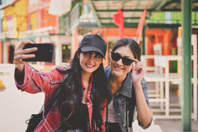 Smiling friends taking selfie while standing on footpath