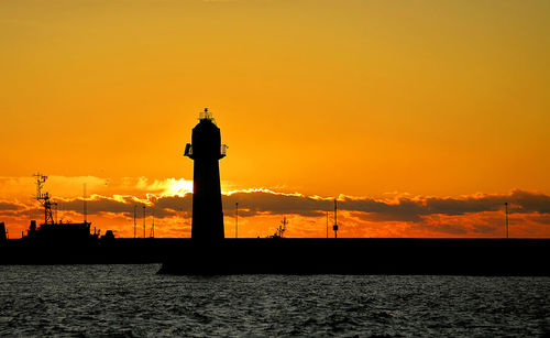 Silhouette of lighthouse at seaside during sunset