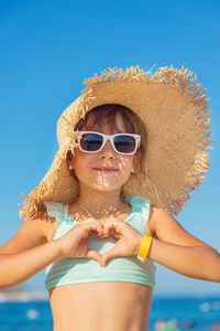 Portrait of young woman wearing sunglasses while standing against clear blue sky