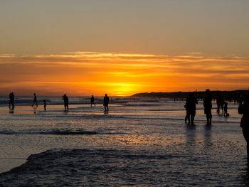 Silhouette people on beach against sky during sunset