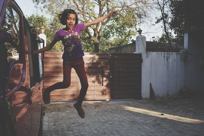 Portrait of girl jumping from car against door