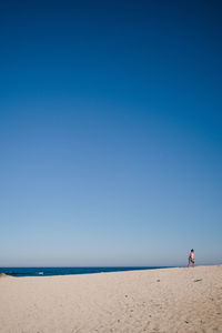 Woman walking on sand at beach against clear blue sky