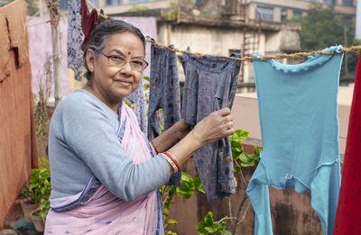 Portrait of a simple looking mature indian woman hanging freshly washed laundry to dry in the sun