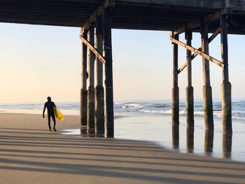 Rear view of man walking on pier at beach