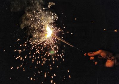 Cropped hand of person holding illuminated sparkler at night